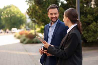 Photo of Coffee to go. Man with paper cup of drink and his business partner during meeting outdoors, space for text