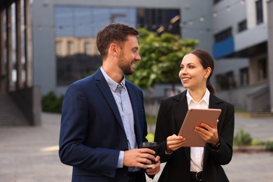 Photo of Coffee to go. Man with paper cup of drink and his business partner during meeting outdoors