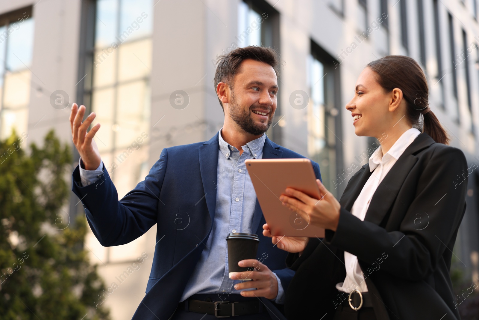 Photo of Coffee to go. Man with paper cup of drink and his business partner during meeting outdoors, low angle view
