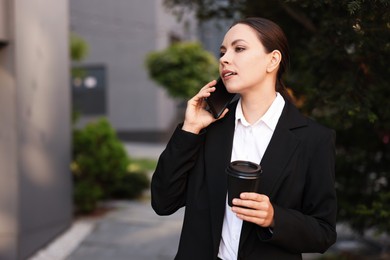 Photo of Coffee to go. Woman with paper cup of drink talking on smartphone outdoors, space for text