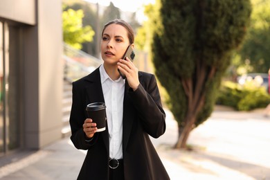 Photo of Coffee to go. Woman with paper cup of drink talking on smartphone outdoors, space for text