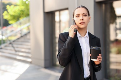 Photo of Coffee to go. Woman with paper cup of drink talking on smartphone outdoors, space for text
