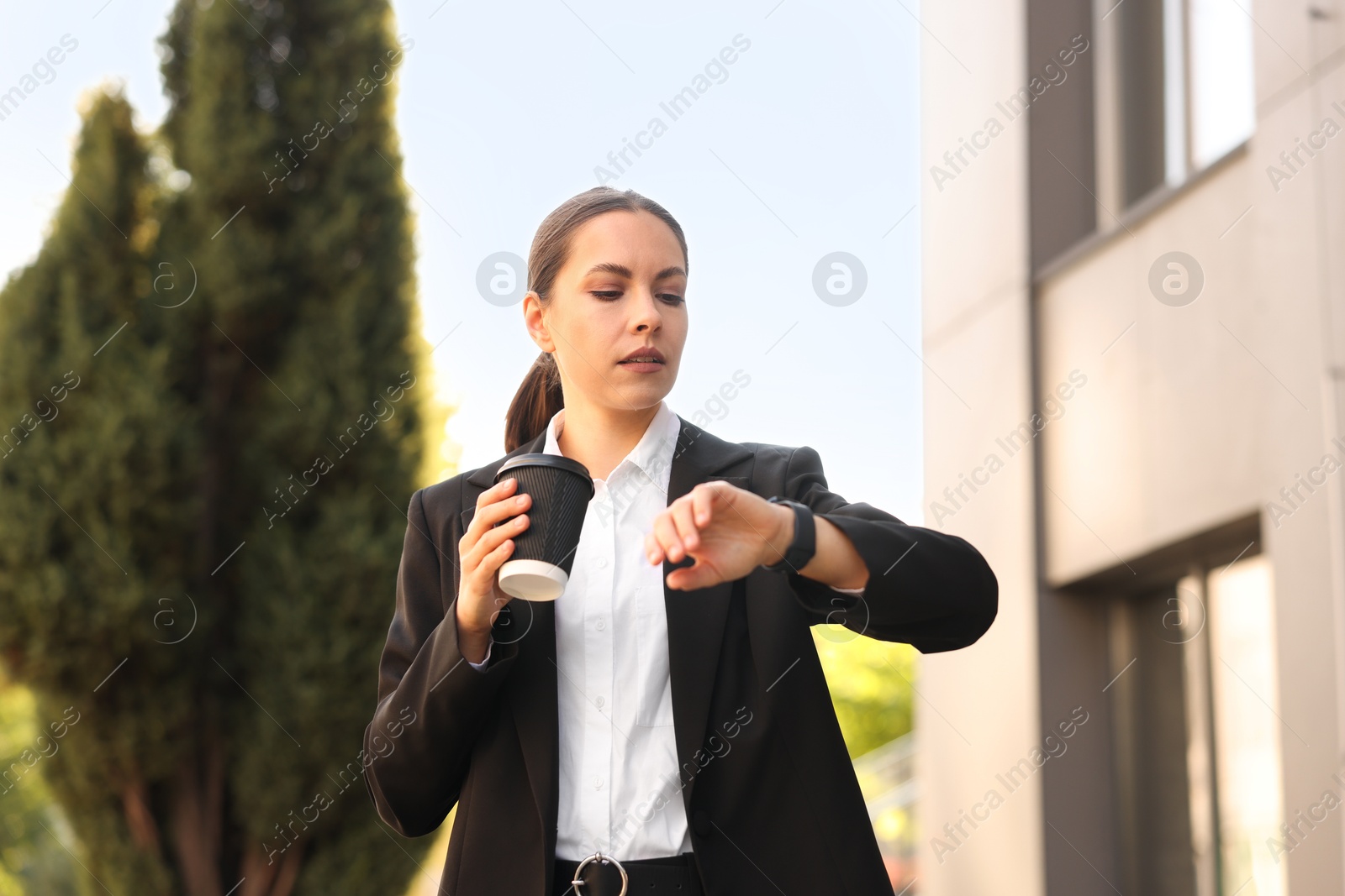 Photo of Coffee to go. Woman with paper cup of drink checking time outdoors, low angle view