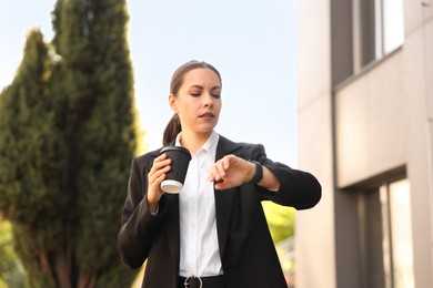 Photo of Coffee to go. Woman with paper cup of drink checking time outdoors, low angle view