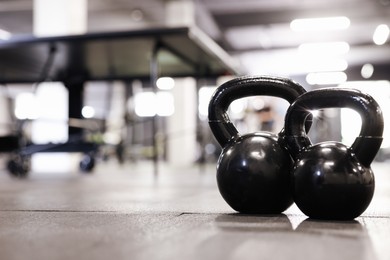 Photo of Black kettlebells on floor in gym, closeup. Space for text