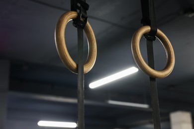 Photo of Gymnastic rings hanging in dark gym. Sport equipment