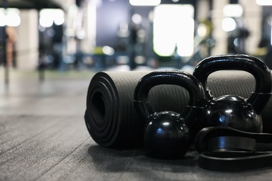 Photo of Black kettlebells and other sport equipment on floor in gym, closeup. Space for text