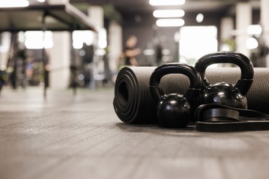 Photo of Black kettlebells and other sport equipment on floor in gym, closeup. Space for text