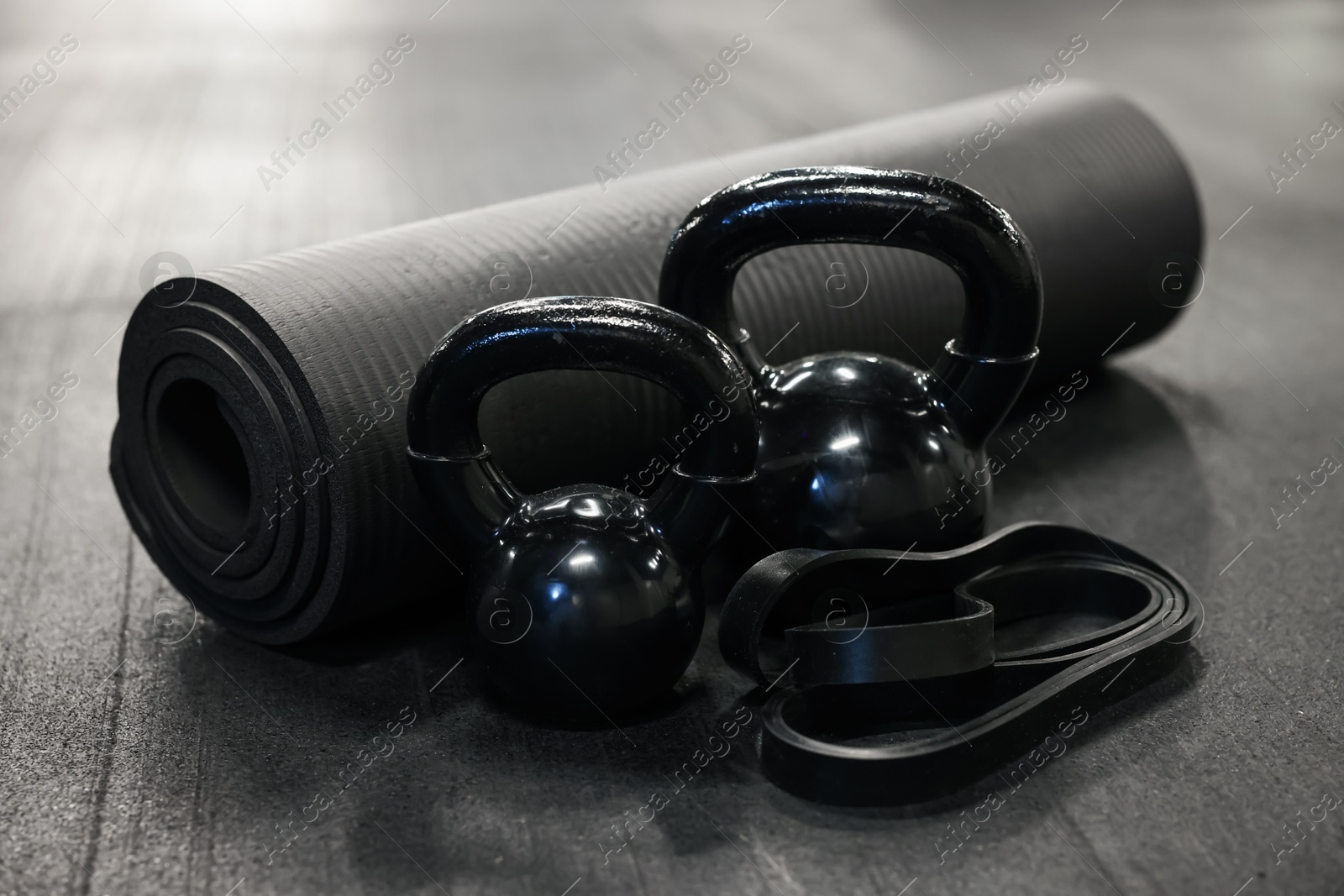 Photo of Black kettlebells and other sport equipment on dark floor in gym, closeup