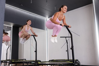 Photo of Smiling women jumping on mini exercise trampolines in fitness studio, low angle view