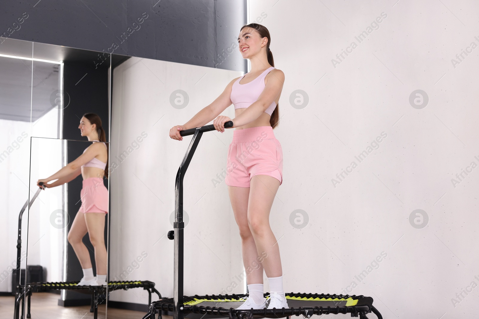 Photo of Smiling woman on mini exercise trampoline near mirror in fitness studio, low angle view