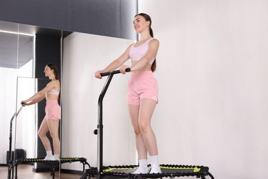 Photo of Smiling woman on mini exercise trampoline near mirror in fitness studio, low angle view