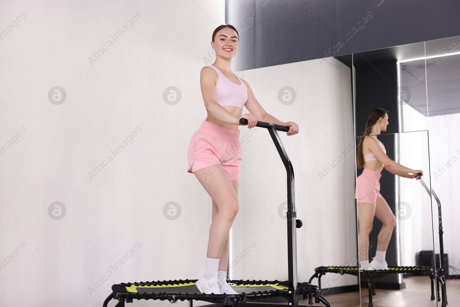Smiling woman on mini exercise trampoline near mirror in fitness studio, low angle view Photo of Smiling woman on mini exercise trampoline near mirror in fitness studio, low angle view