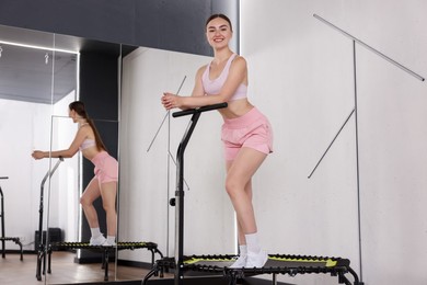 Photo of Smiling woman on mini exercise trampoline near mirror in fitness studio, low angle view