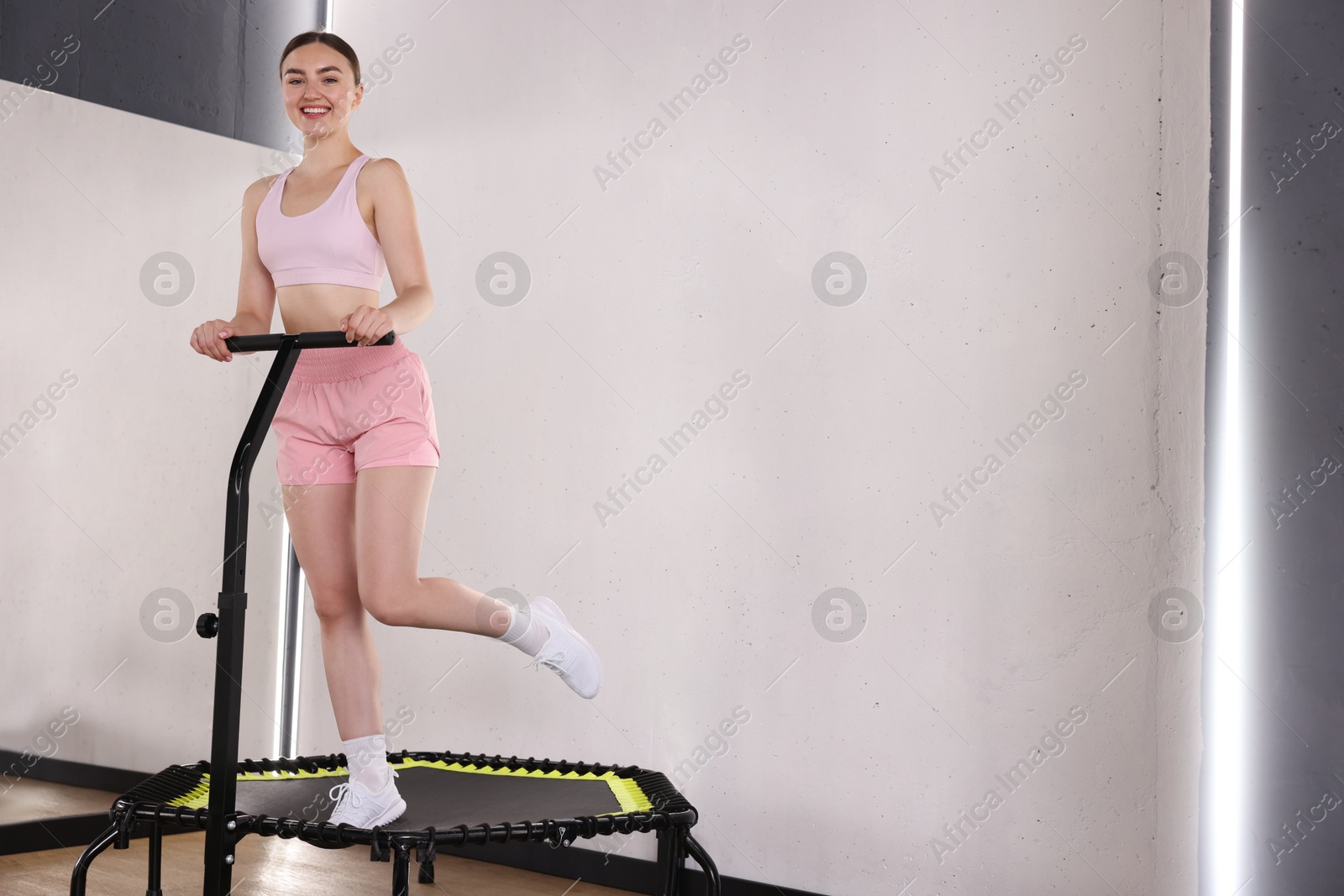 Smiling woman on mini exercise trampoline in fitness studio, low angle view. Space for text Photo of Smiling woman on mini exercise trampoline in fitness studio, low angle view. Space for text