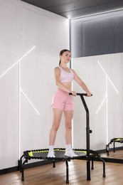 Photo of Young woman on mini exercise trampoline near mirror in fitness studio
