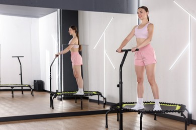 Photo of Smiling woman on mini exercise trampoline near mirror in fitness studio. Space for text