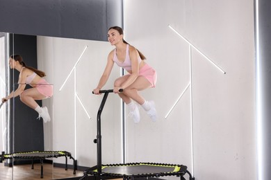 Photo of Smiling woman jumping on mini exercise trampoline near mirror in fitness studio