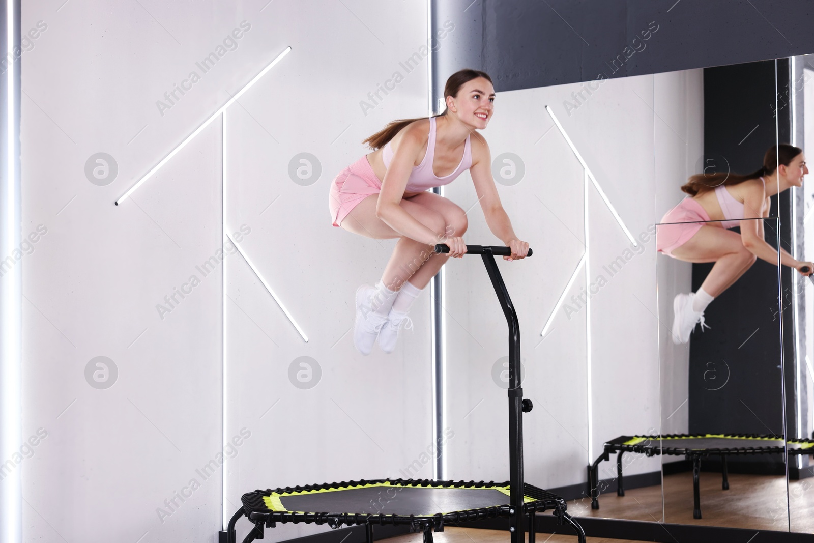 Smiling woman jumping on mini exercise trampoline near mirror in fitness studio Photo of Smiling woman jumping on mini exercise trampoline near mirror in fitness studio