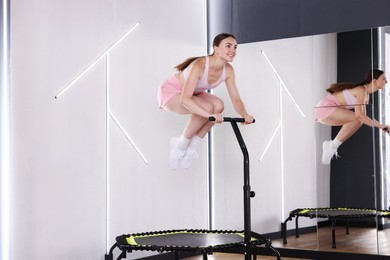 Photo of Smiling woman jumping on mini exercise trampoline near mirror in fitness studio