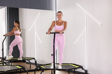 Photo of Smiling woman on mini exercise trampoline near mirror in fitness studio
