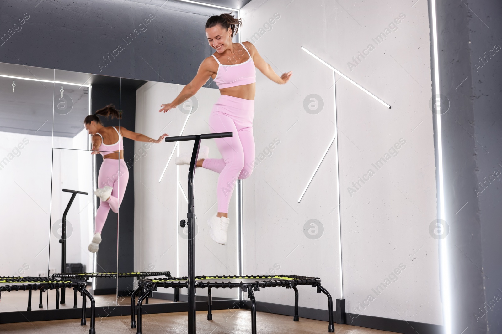Smiling woman jumping on mini exercise trampoline near mirror in fitness studio, low angle view Photo of Smiling woman jumping on mini exercise trampoline near mirror in fitness studio, low angle view