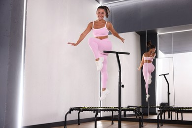 Photo of Smiling woman jumping on mini exercise trampoline near mirror in fitness studio, low angle view