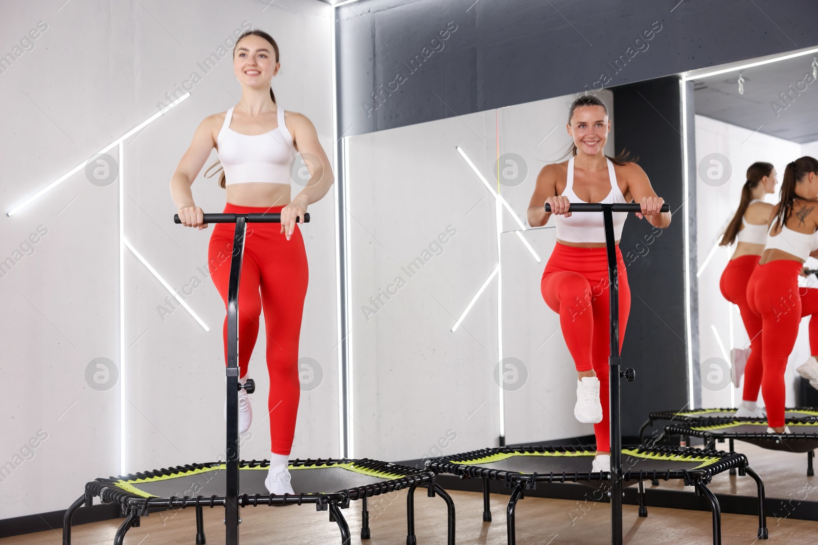 Photo of Smiling women training on mini exercise trampolines in fitness studio, low angle view