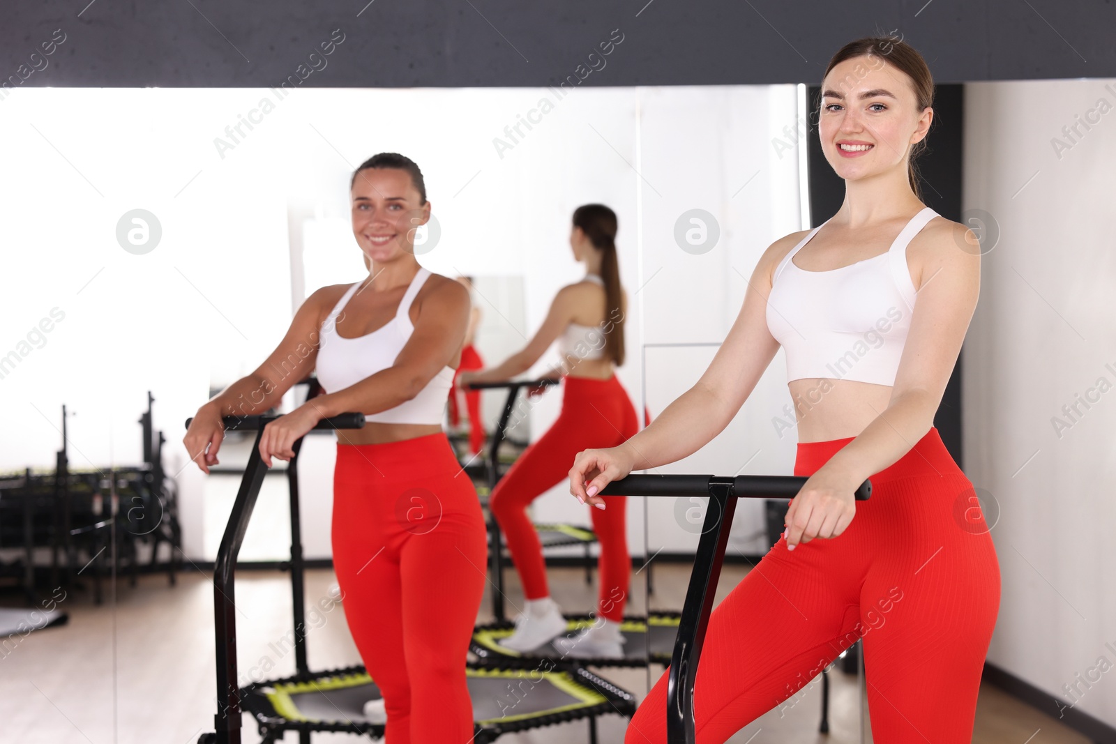 Smiling women on mini exercise trampolines near mirror in fitness studio Photo of Smiling women on mini exercise trampolines near mirror in fitness studio