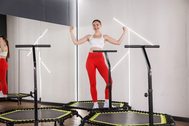 Photo of Smiling woman showing her biceps on mini exercise trampoline in fitness studio, low angle view