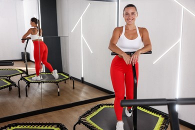 Photo of Smiling woman on mini exercise trampoline near mirror in fitness studio. Space for text