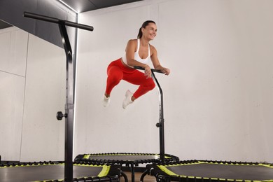 Photo of Smiling woman jumping on mini exercise trampoline in fitness studio, low angle view