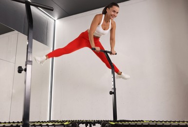 Photo of Smiling woman jumping on mini exercise trampoline in fitness studio, low angle view