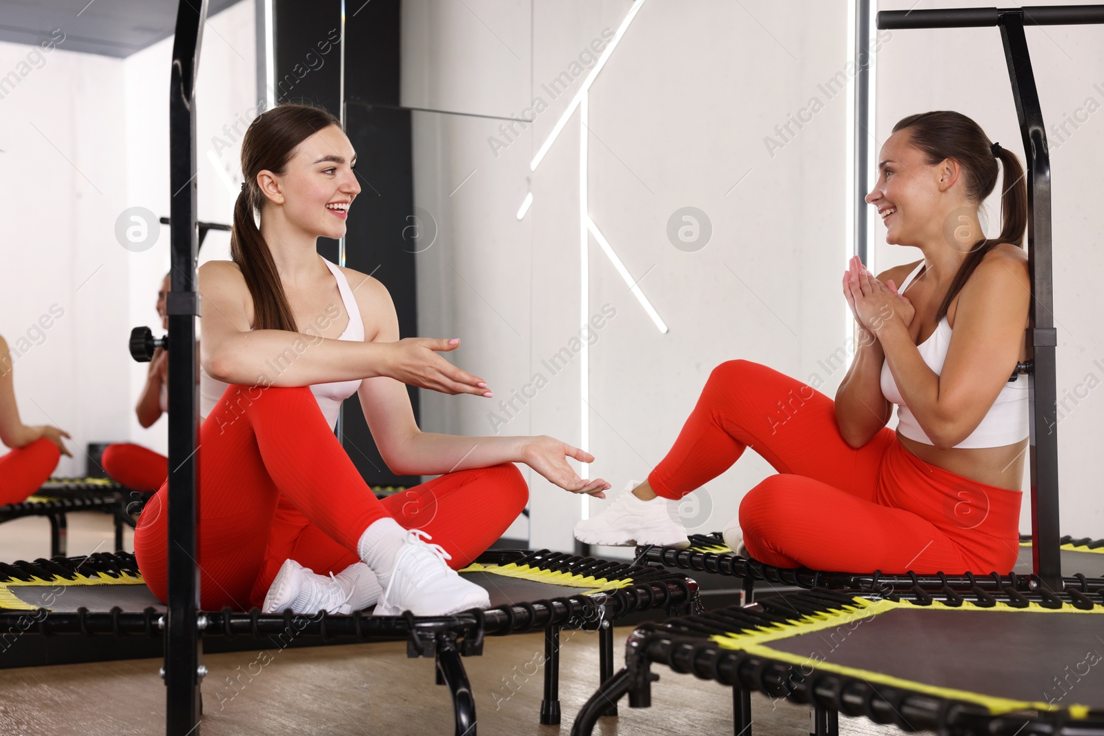Smiling women talking on mini exercise trampolines in fitness studio Photo of Smiling women talking on mini exercise trampolines in fitness studio