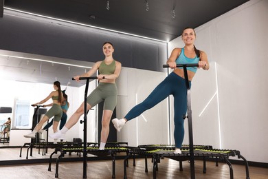 Photo of Smiling women training on mini exercise trampolines in fitness studio, low angle view