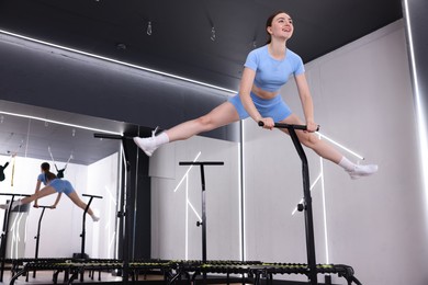 Photo of Smiling woman jumping on mini exercise trampoline in fitness studio, low angle view. Space for text