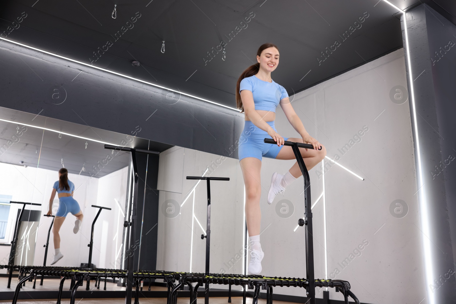 Photo of Smiling woman jumping on mini exercise trampoline in fitness studio, low angle view. Space for text