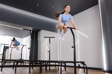Photo of Smiling woman jumping on mini exercise trampoline in fitness studio, low angle view. Space for text