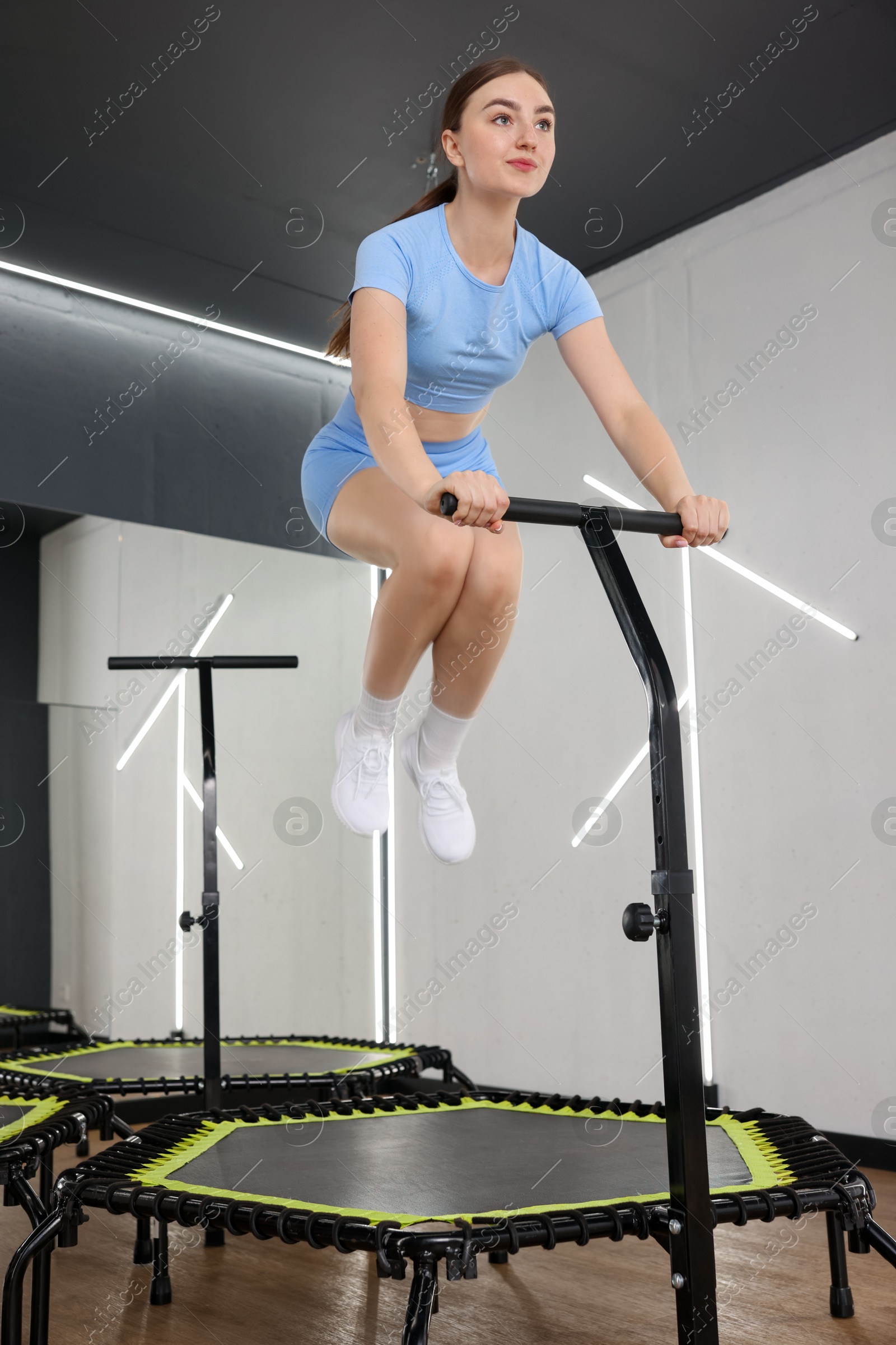 Photo of Young woman jumping on mini exercise trampoline in fitness studio, low angle view