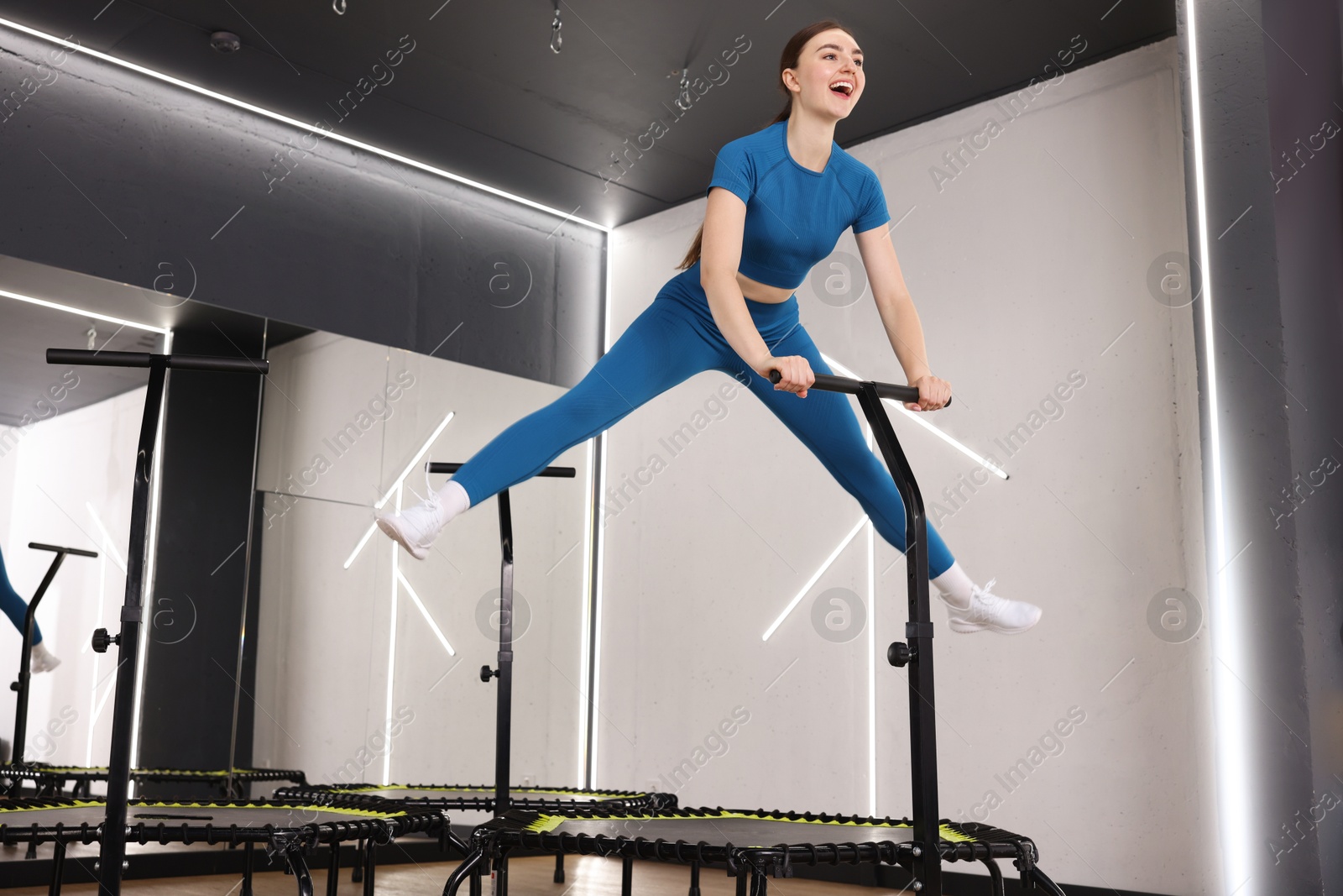Happy woman jumping on mini exercise trampoline in fitness studio, low angle view Photo of Happy woman jumping on mini exercise trampoline in fitness studio, low angle view