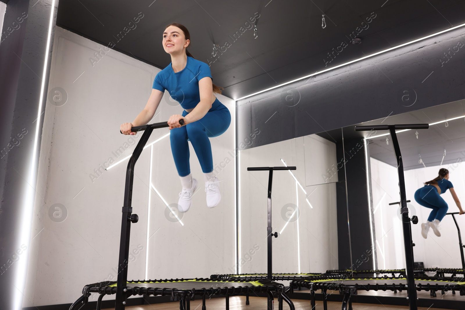Smiling woman jumping on mini exercise trampoline in fitness studio, low angle view Photo of Smiling woman jumping on mini exercise trampoline in fitness studio, low angle view