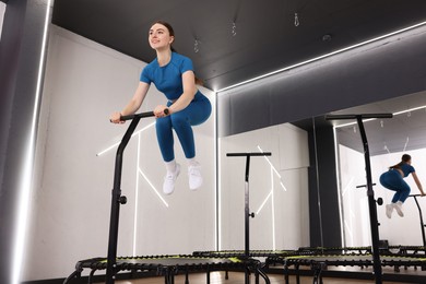Photo of Smiling woman jumping on mini exercise trampoline in fitness studio, low angle view