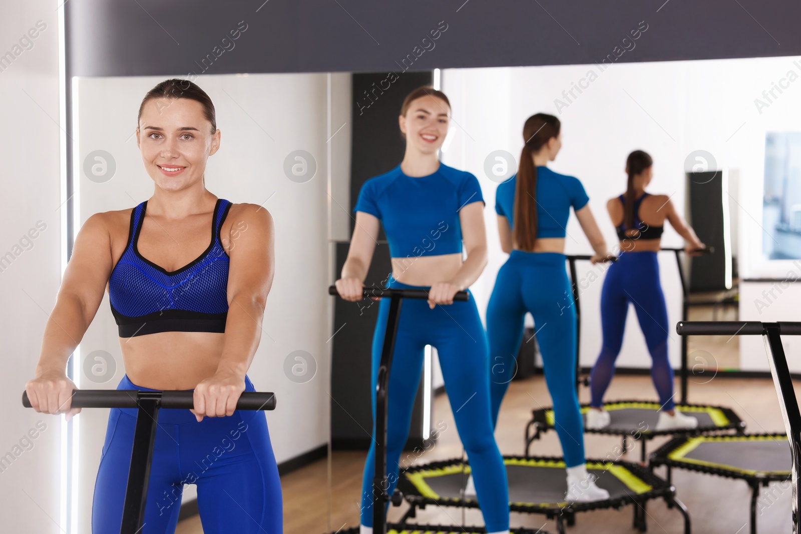 Smiling women on mini exercise trampolines near mirror in fitness studio Photo of Smiling women on mini exercise trampolines near mirror in fitness studio
