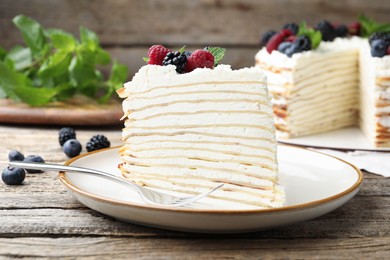 Photo of Piece of tasty crepe cake with berries served on wooden table, closeup