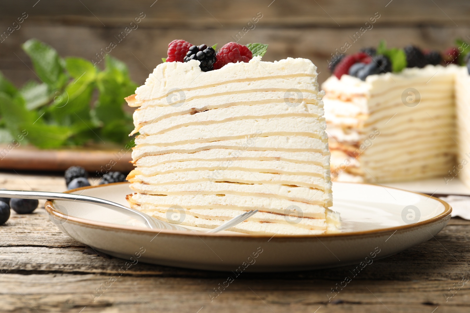 Photo of Piece of tasty crepe cake with berries served on wooden table, closeup