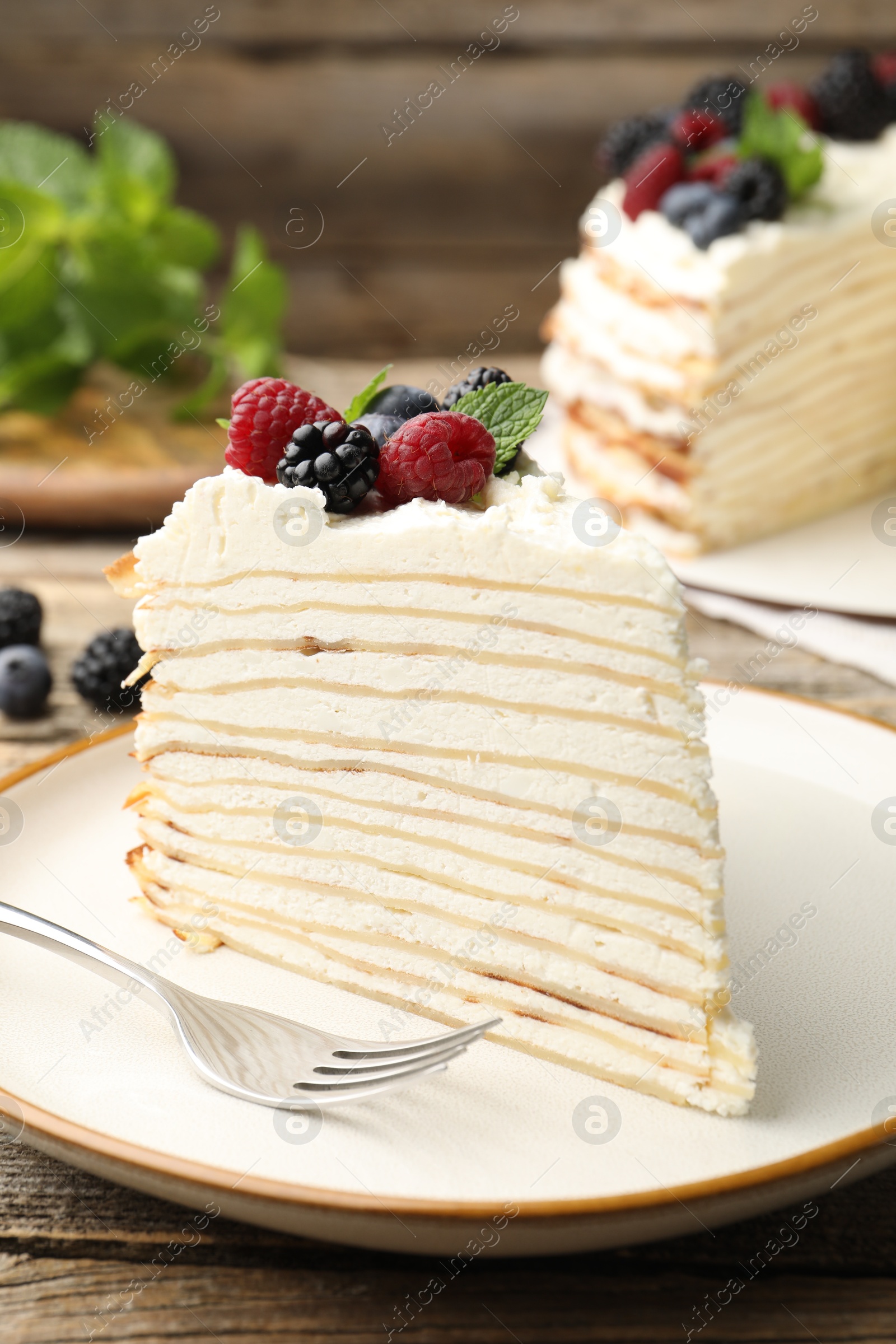 Photo of Piece of tasty crepe cake with berries served on wooden table, closeup