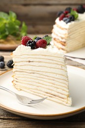 Photo of Piece of tasty crepe cake with berries served on wooden table, closeup
