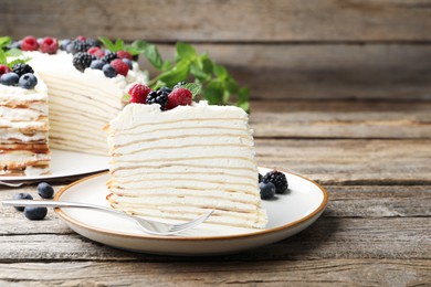Photo of Piece of tasty crepe cake with berries served on wooden table, closeup. Space for text