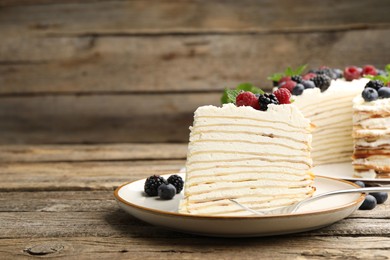 Photo of Piece of tasty crepe cake with berries served on wooden table, closeup. Space for text