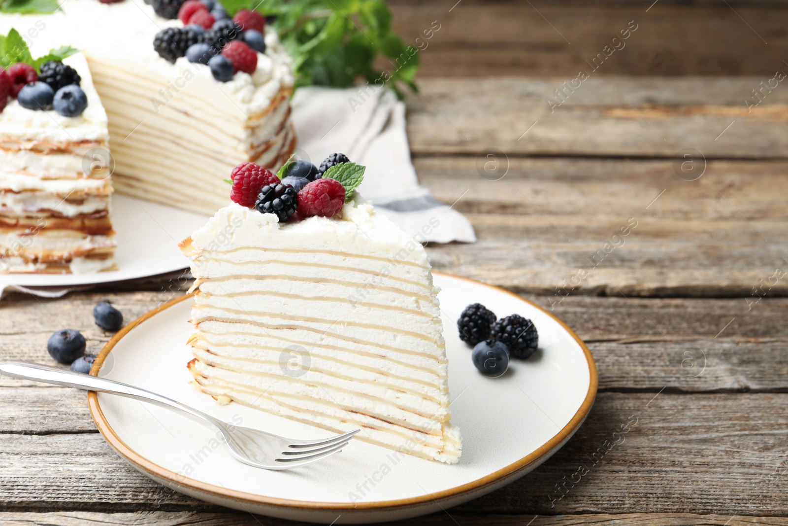 Photo of Piece of tasty crepe cake with berries served on wooden table, closeup. Space for text